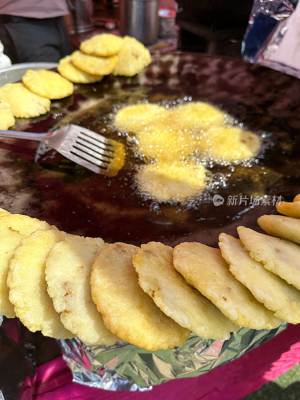 印度街头小吃摊Tawa(又大又平的金属平底锅)煮着食用油，油炸着aloo tikki(土豆饼)，开槽的金属锅铲，重点在前景